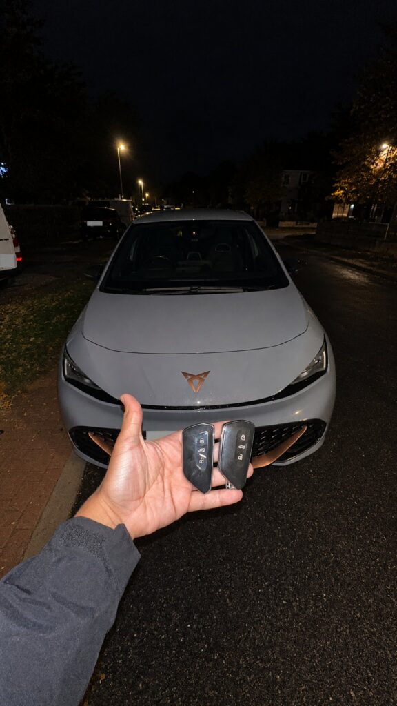 Two key fobs held in front of a 2023 Cupra electric car after a spare key service.