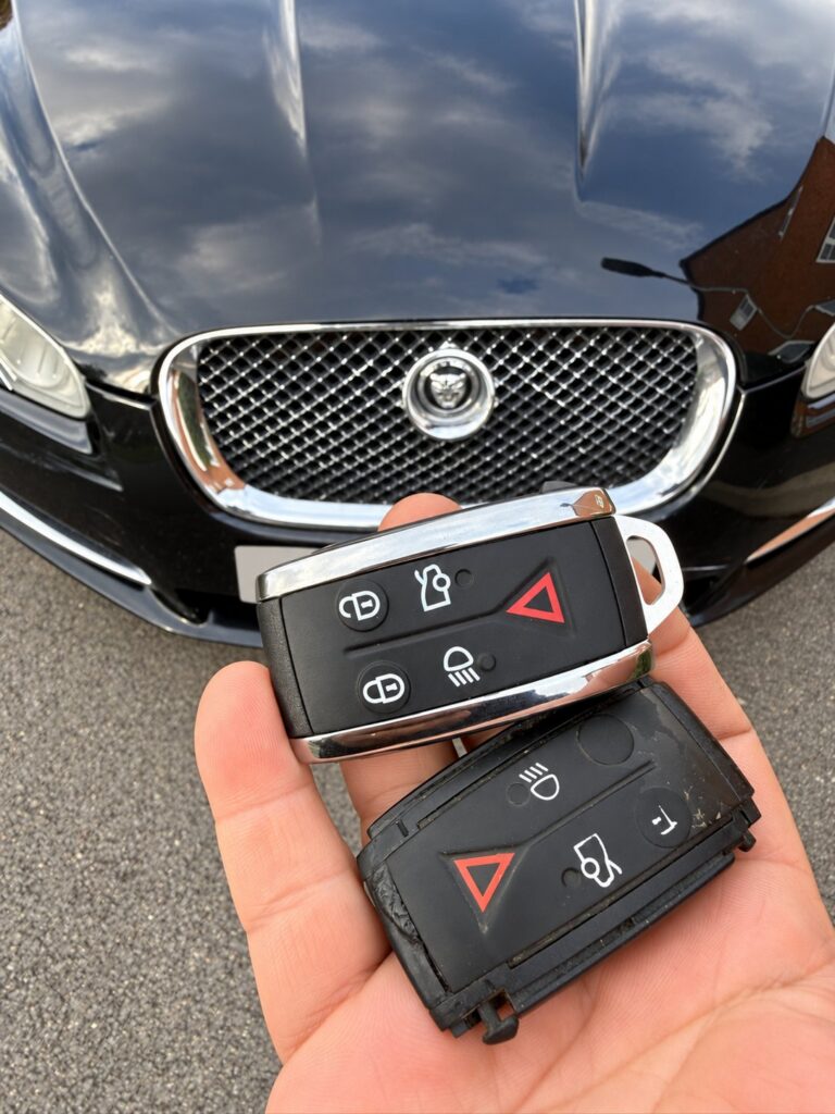Damaged old Jaguar key beside a new replacement key, with the vehicle grille in the background.